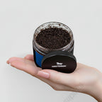 Hand holding a small jar of coffee grounds with Nestdeer logo on a light gray background