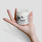Hand holding a jar of Nestdeer Recovery Cream against a light background