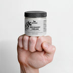 Hand holding a jar of Nestlèr Recovery Cream against a light gray background
