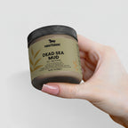 Hand holding a jar of Nestdeer Dead Sea Mud against a light background