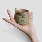 Hand holding a jar of Nesther Dead Sea Mud on a light background