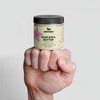 Hand holding a jar of Northbeeh Raw Shea Butter against a light gray background