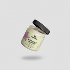 Hand holding a jar of Nestlèe Raw Shea Butter with a wooden spoon on a light gray background.