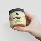 Hand holding a jar of Nestder Raw Shea Butter against a light background