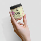 Hand holding a jar of Raw Shea Butter against a light background